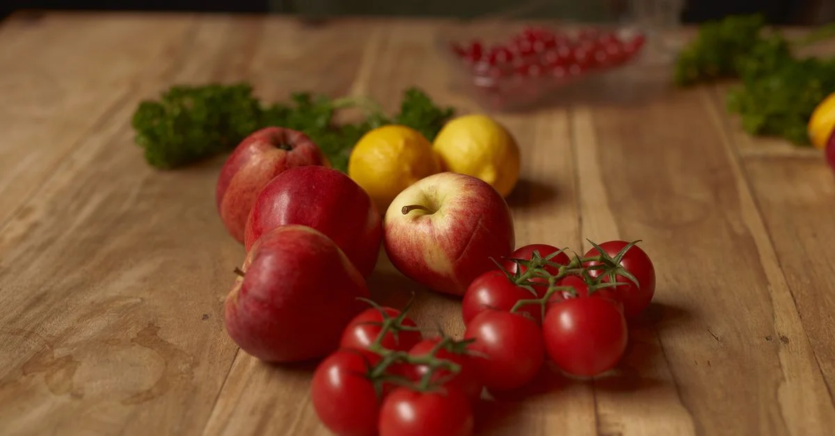 Mélange coloré de pommes, citrons, tomates cerises et persil sur une table en bois rustique.