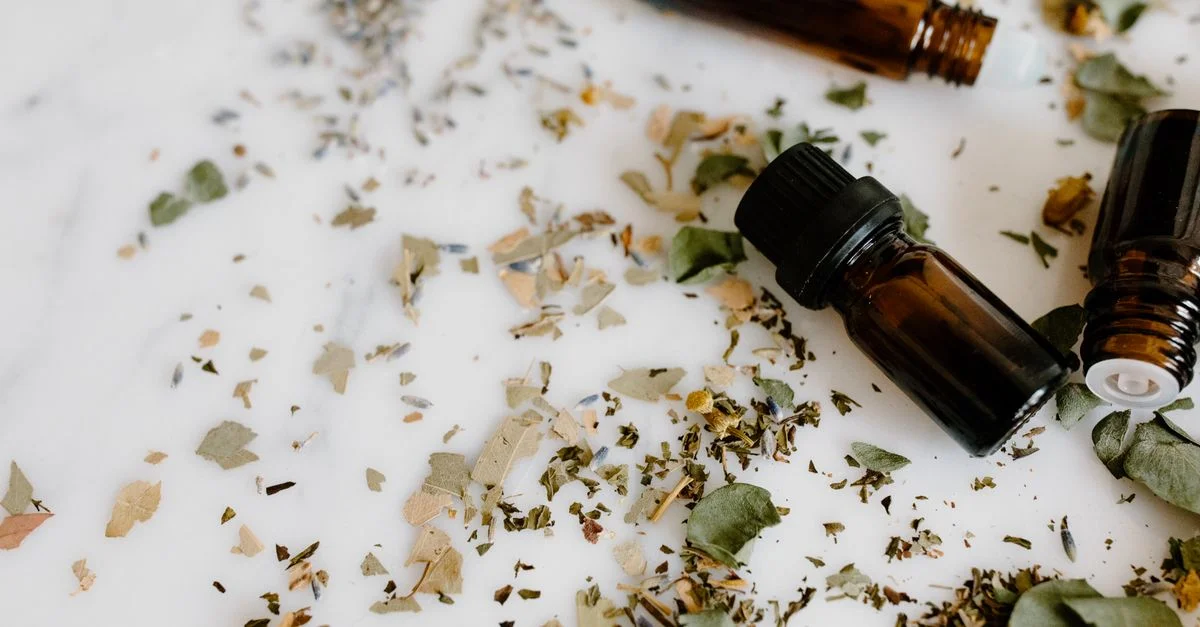 Installation d'aromathérapie avec des flacons d'huiles essentielles et des herbes sèches sur une surface blanche pour la guérison holistique.
