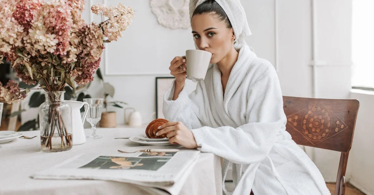 Une femme prenant son petit déjeuner avec un café et un croissant dans un cadre intérieur confortable.